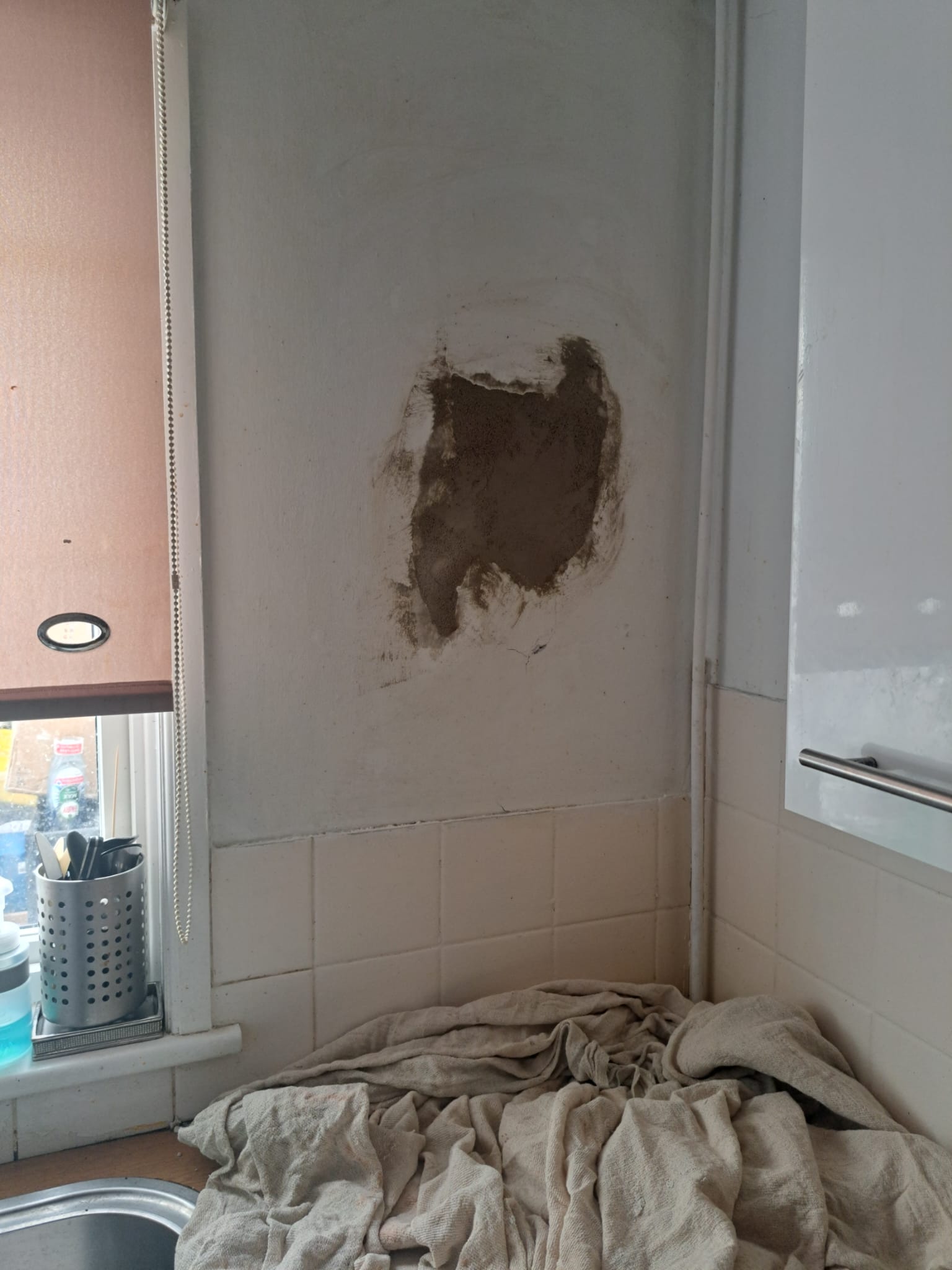 Kitchen wall with a patch of damaged plaster above the tiled splashback