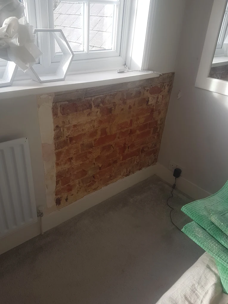 Bare brick patch above a radiator beneath the windowsill