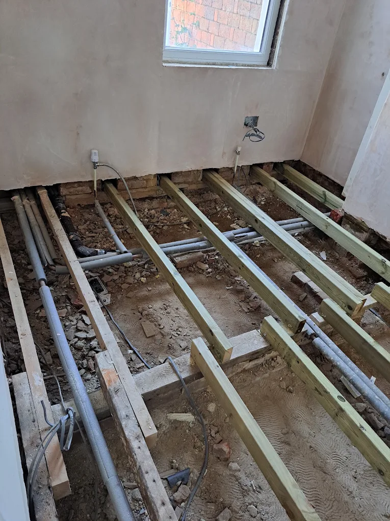 Floor joists exposed with pipework running underneath during floor renewal